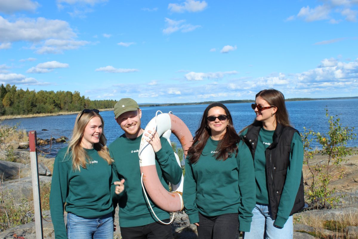 Fyra personer ur Evitys supportteam i gröna Evity-tröjor vid vattnet. En av dem håller en livboj.
